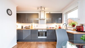A modern kitchen with grey cabinets, a built-in oven, and a glass dining table. - York City Centre Luxurious Apartment with FREE ONSITE PARKING! (York)