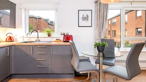 A modern kitchen with grey cabinets, a red kettle, and a glass table with two chairs. - York City Centre Luxurious Apartment with FREE ONSITE PARKING! (York)