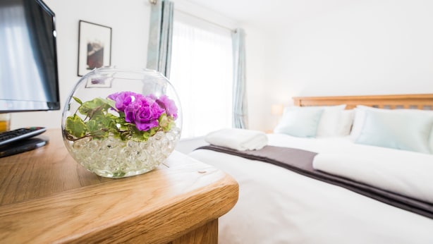 A hotel room with a bed, a TV, and a glass vase with flowers on a wooden table. - York City Centre Luxurious Apartment with FREE ONSITE PARKING! (York)