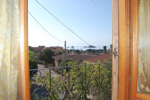 Ein Balkon mit schmiedeeisernen Geländern mit Blick auf eine Küstenstadt, mit Häusern und dem Meer.