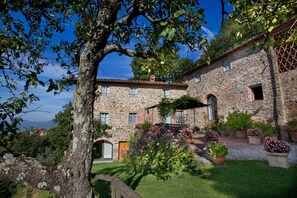 Un edificio in pietra con numerose finestre e un giardino curato, decorato con diverse piante in vaso.