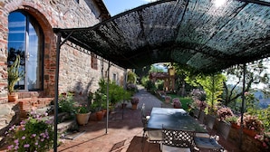 Une terrasse extérieure avec une table et des chaises, entourée de plantes en pot et d’un bâtiment en pierre.