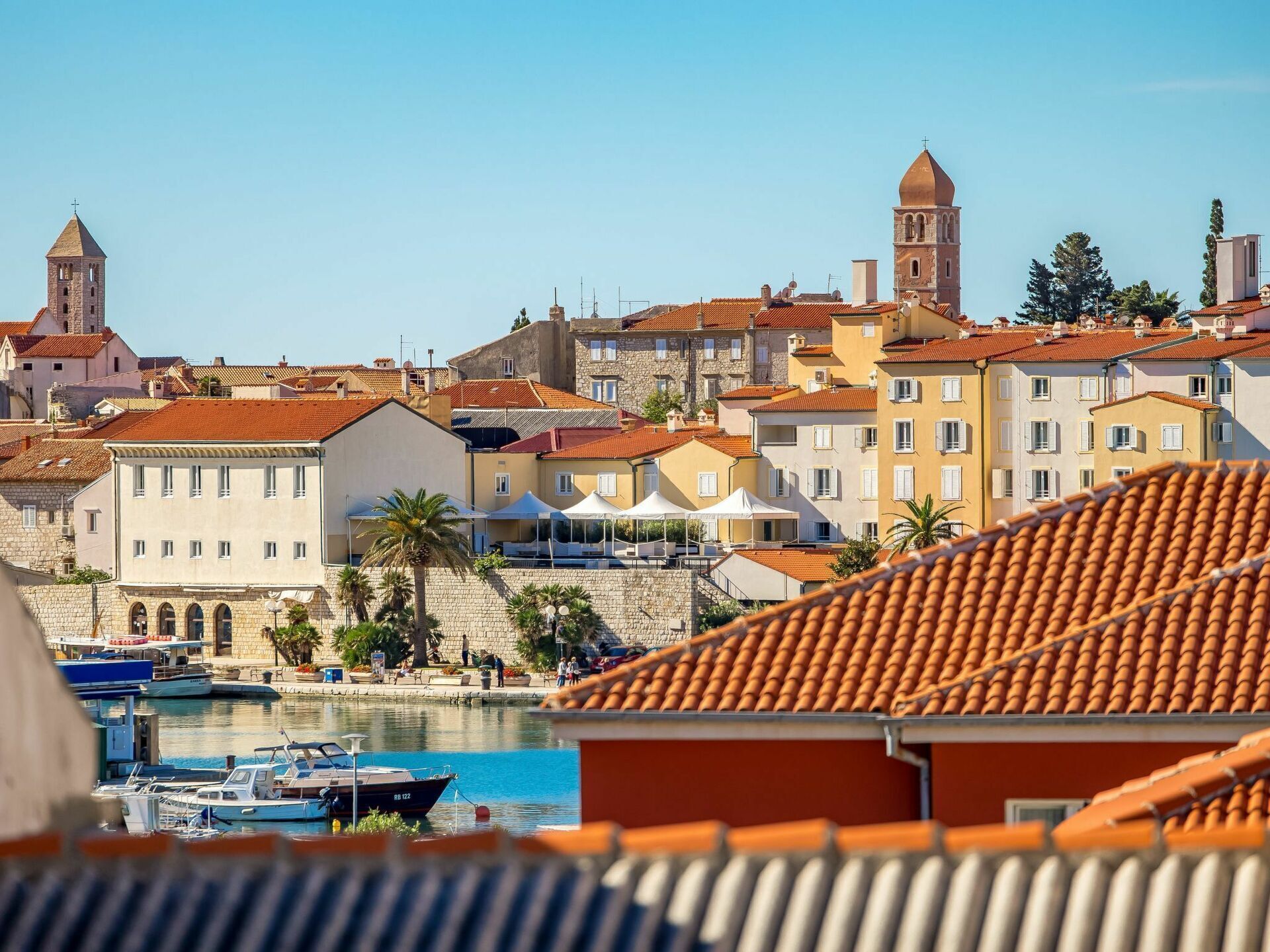 A coastal town with historic buildings, a marina with boats, and a prominent tower.