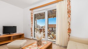 Un salon moderne doté d’un téléviseur à écran plat, de meubles en bois, d’un canapé et d’un balcon offrant une vue sur les immeubles.