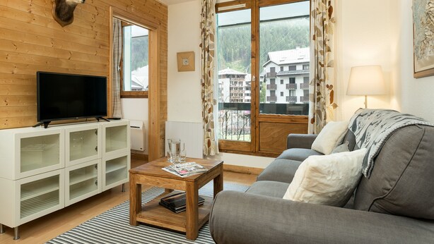 A living room with a television, a sofa, a coffee table, and a view of a building through a window.