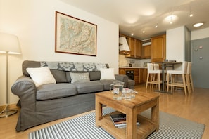 A modern living room with a grey sofa, a wooden coffee table, and a kitchen area in the background.