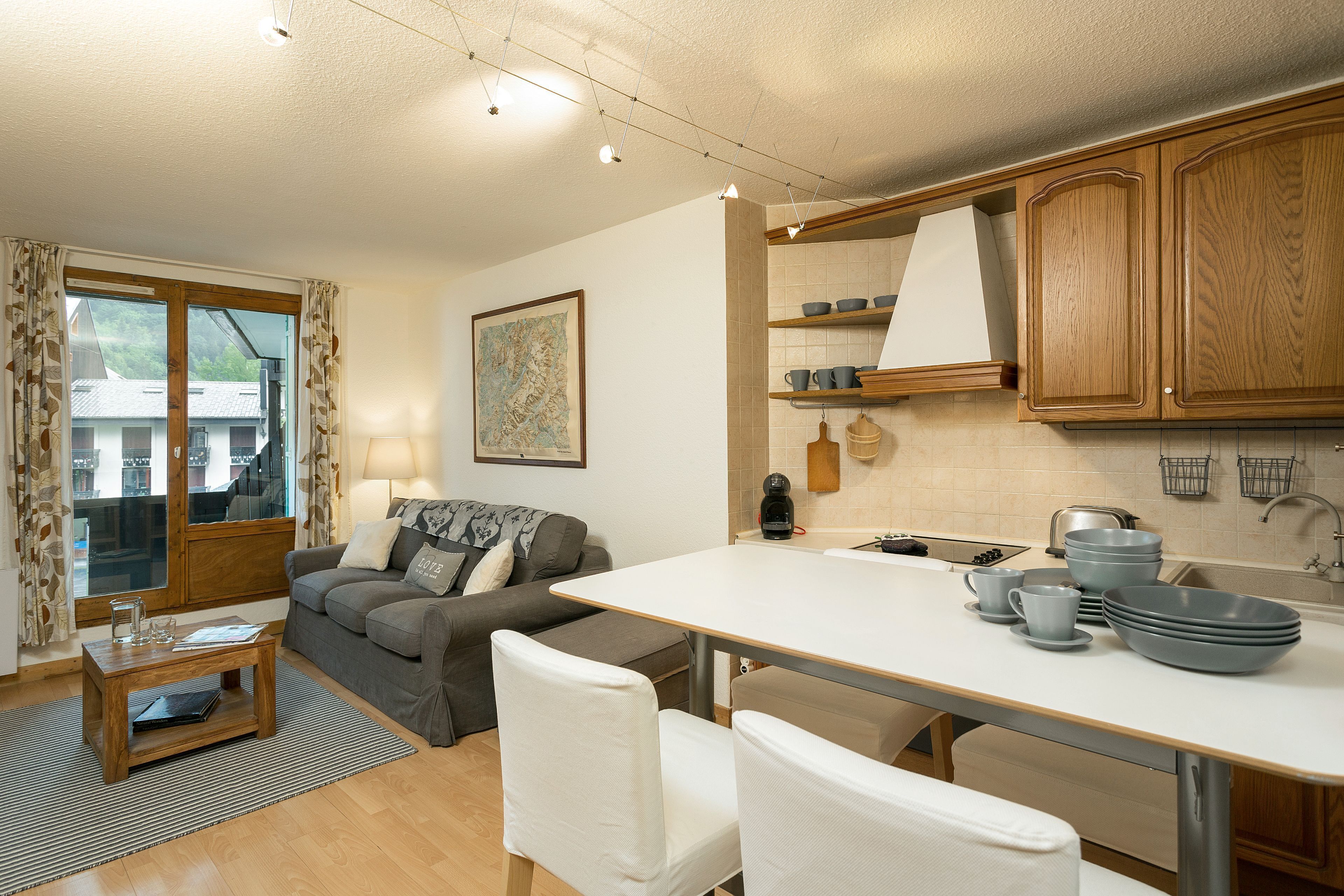 Una cocina moderna con armarios de madera, una encimera blanca y una zona de comedor con una mesa y sillas.
