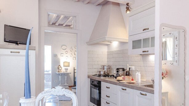A kitchen with white cabinets, a stove, and a sink. There are decorative plates on the wall and a mirror above the sink. - Convenient Home close to Train Station and Parking (Lucca)