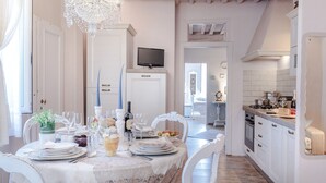 A dining area with a table set for six, a chandelier, and a kitchen visible in the background. - Convenient Home close to Train Station and Parking (Lucca)