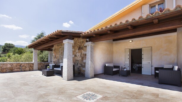 Un patio al aire libre con suelo de piedra, una estructura de pérgola y mobiliario exterior.