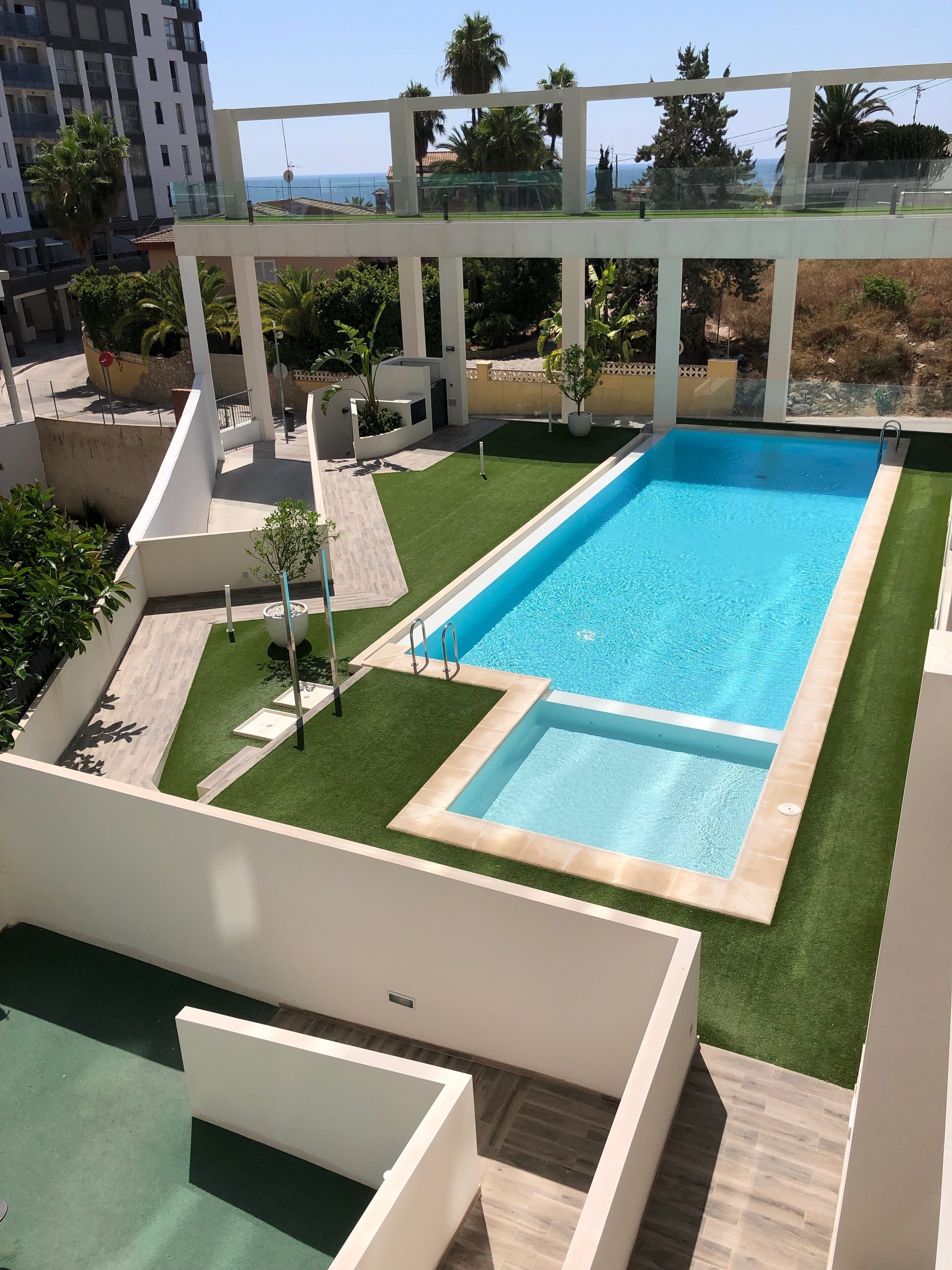 A rooftop pool with a view of the sea, surrounded by greenery and modern architecture.