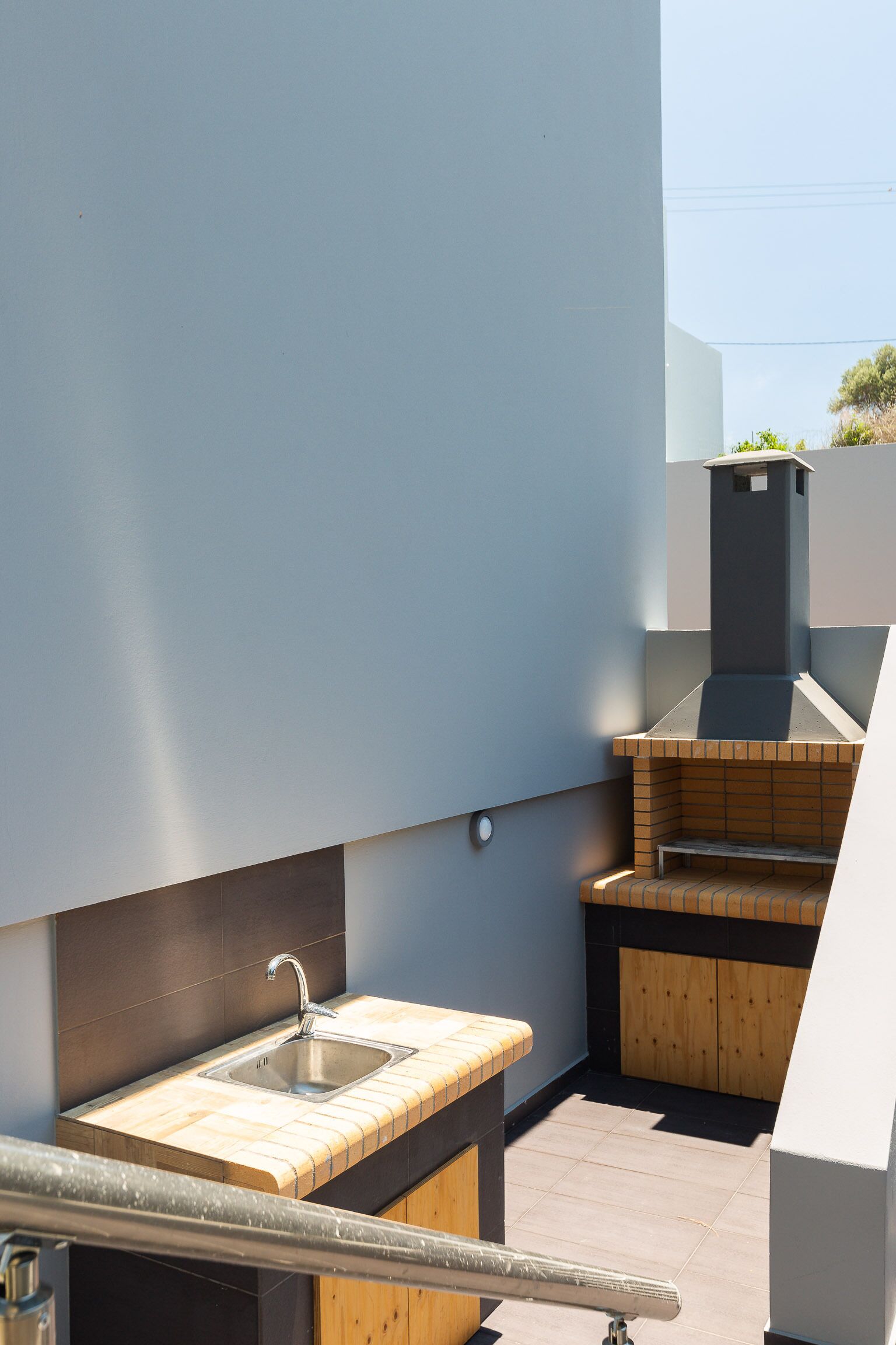 Un área compacta de cocina exterior con un fregadero y una parrilla, delimitada por un muro bajo.