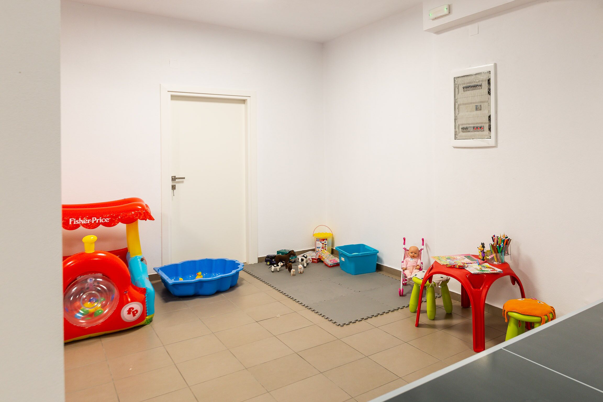 A children's play area with a red toy tractor, blue play bins, and a small table with toys.