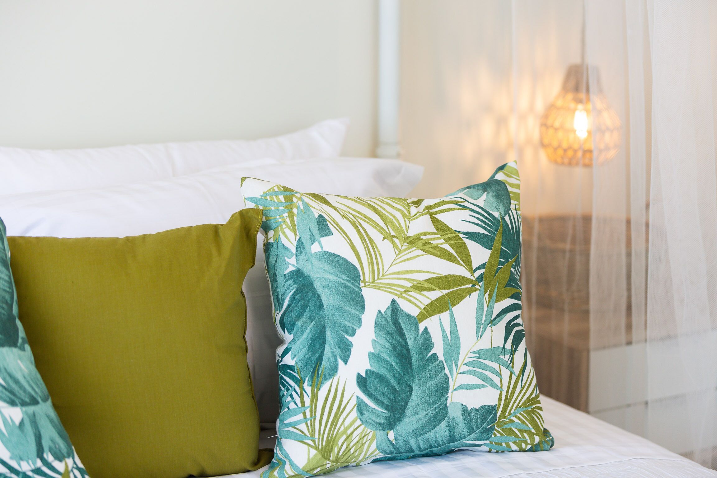 A bed with white bedding and two pillows, one with a leaf pattern and the other solid green.