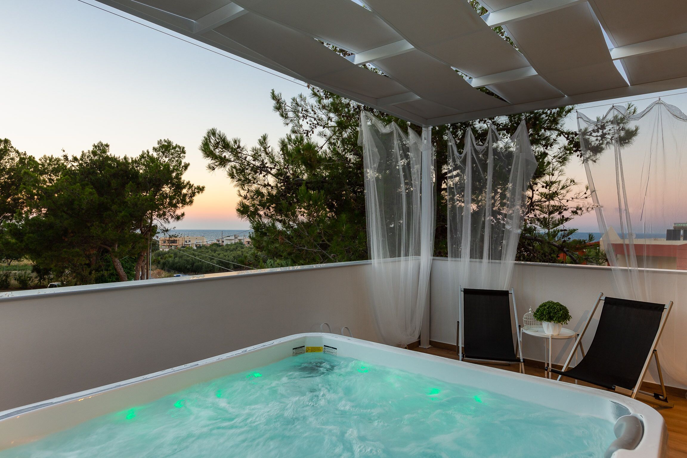 A rooftop terrace with a hot tub, two chairs, and a view of the sunset.