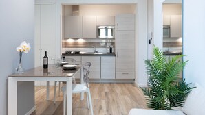 Ett modernt kök med vita köksskåp, en matplats med ett vitt bord och stolar samt en stor spegel på väggen.