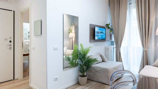 Ett modernt, väl upplyst rum med en soffa, ett matbord, en krukväxt och en tv som är monterad på väggen.