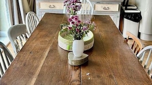 Une salle à manger avec une table en bois, des chaises, un vase de fleurs, un buffet vert contenant de la verrerie et une horloge au mur.