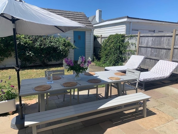 En udendørs terrasse med et hvidt bord dækket til fire personer, omgivet af loungesenge.