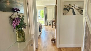 Un couloir doté d’un plancher en bois, une commode blanche avec des tiroirs, un vase rempli de fleurs et un tableau accroché au mur.