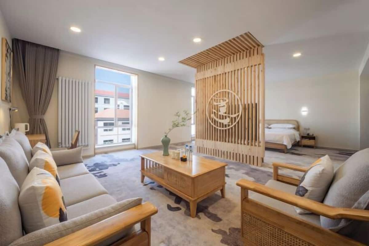A modern hotel room with a sofa set, a wooden coffee table, a bed, and a decorative wall panel.