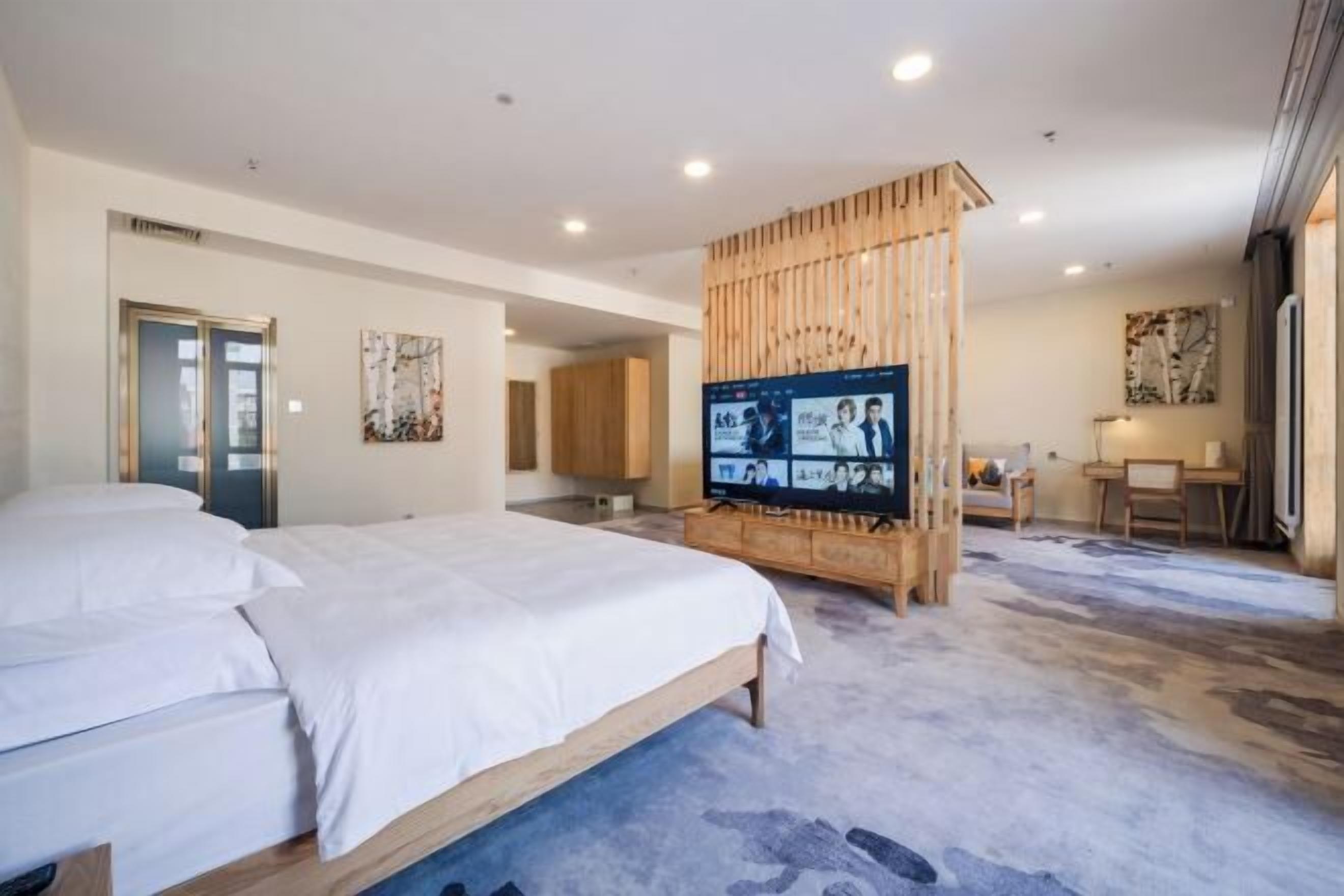A modern hotel room with a large bed, a wooden partition, a television, and a desk area.