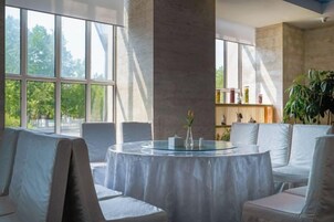 Una mesa redonda con sillas en una habitación con ventanas amplias y una estantería.