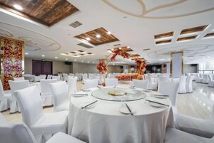 Un salón de banquetes con mesas redondas, sillas blancas y un arco decorativo central.