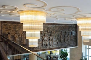 Un vestíbulo con una imponente escalera, un mural grande en la pared y varios candelabros.