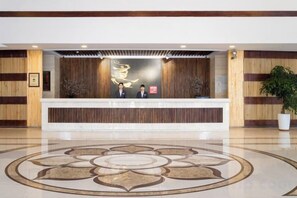 A reception area with a reception desk, two staff members, a decorative wall, and a patterned floor. - Eerguna Hotel (EERGUNA)