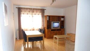 A living room with a wooden dining table, chairs, a TV on a wooden cabinet, and a sofa. - Chez Nônô - 4 bedroom, 2 toilet, in the city (Ponta Delgada)