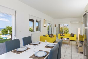 A bright living area with a yellow sofa, a dining table set with plates and glasses, and a view of the outdoors.