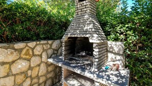 Un four extérieur en pierre, doté d’une cheminée, entouré de verdure.