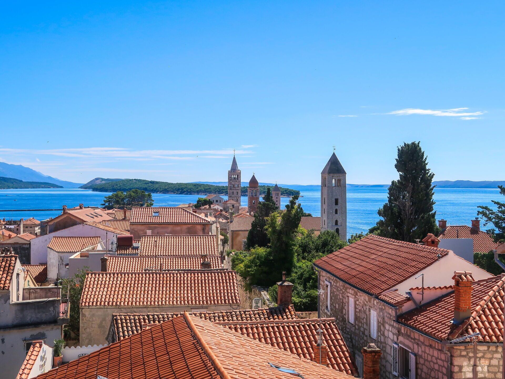A coastal town with terracotta-roofed buildings, a prominent church tower, and a clear view of the sea.