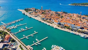 Vue aérienne d’une ville côtière avec un port de plaisance, des bâtiments aux toits recouverts de tuiles rouges et une mer d’un bleu limpide.