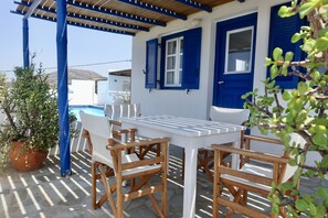 A patio with a white table and wooden chairs, a blue door, and a potted plant.
