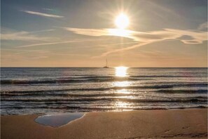 Eine Strandansicht, im Hintergrund ein Boot und die Sonne spiegelt sich im Wasser.