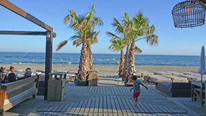 Una terraza de madera con palmeras, una playa al fondo y un niño jugando.