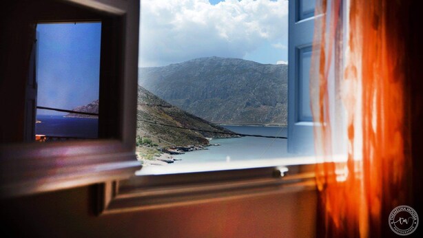 A window view of a mountainous landscape with a lake, a clear sky, and a wooden interior.