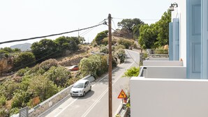 A white car driving on a winding road with a steep incline, surrounded by greenery and a mountainous backdrop.