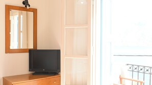 A room with a wooden dresser, a flat-screen TV, a mirror, and a sliding glass door leading to a balcony with a chair.