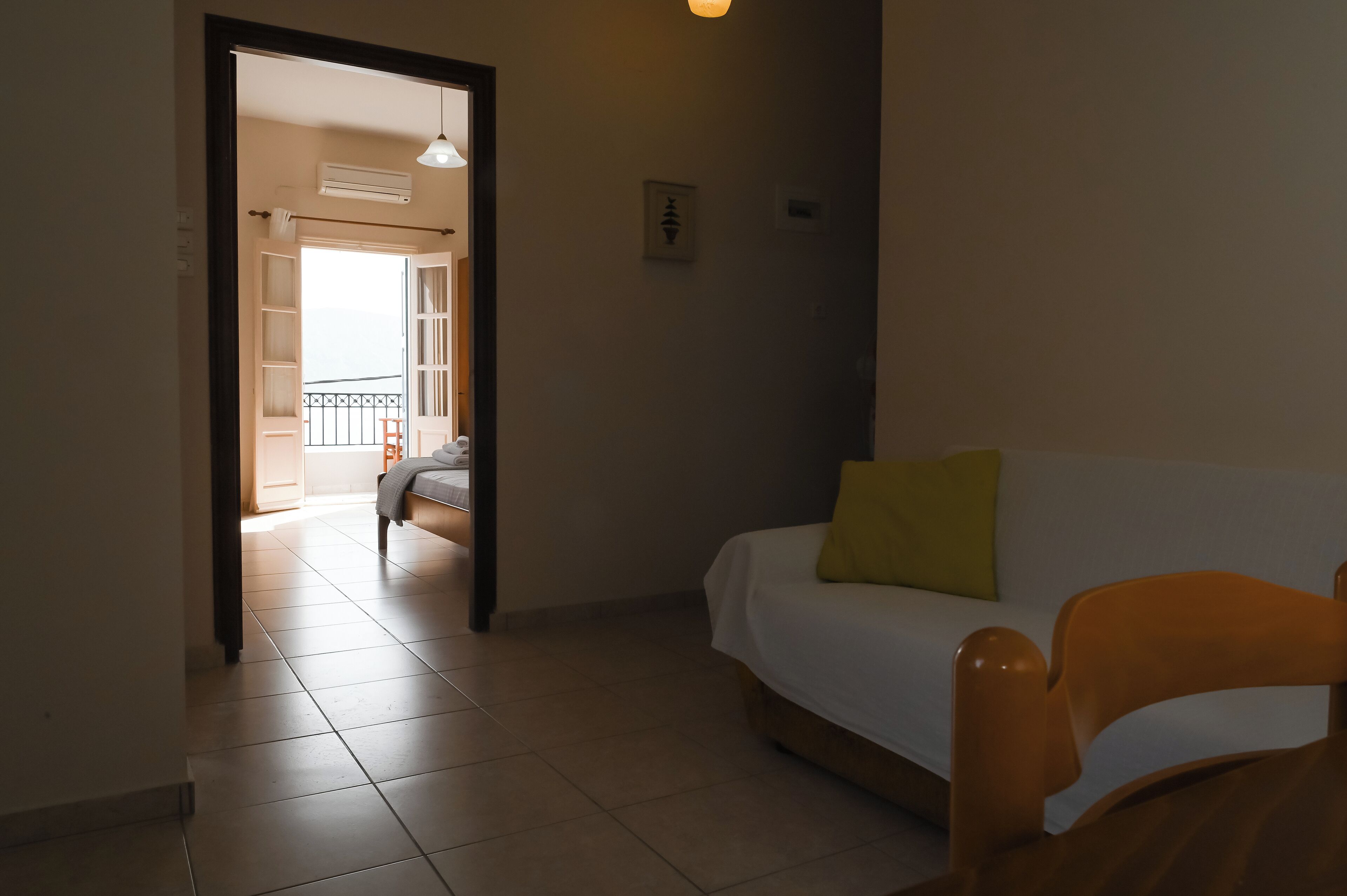 A room with a bed, a wooden chair, and a white sofa with a yellow pillow.