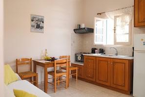 Une cuisine compacte avec des meubles en bois, un four à micro-ondes et un évier. On y trouve une table à manger avec des chaises et une petite fenêtre avec des rideaux.