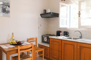 Una cocina con una mesa de madera, sillas, estufa, lavaplatos y una ventana con cortinas.
