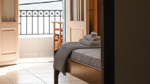 A bedroom with a bed, a chair, and a balcony with a railing.