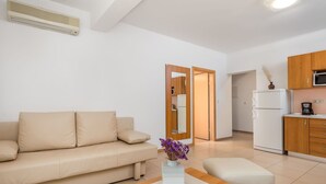 A modern living room with a beige sofa, a wooden coffee table, and a kitchen area with a refrigerator and microwave.