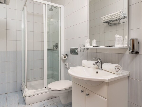 Un baño moderno con ducha envuelta en vidrio, inodoro, lavabo con espejo y perchero para toallas.