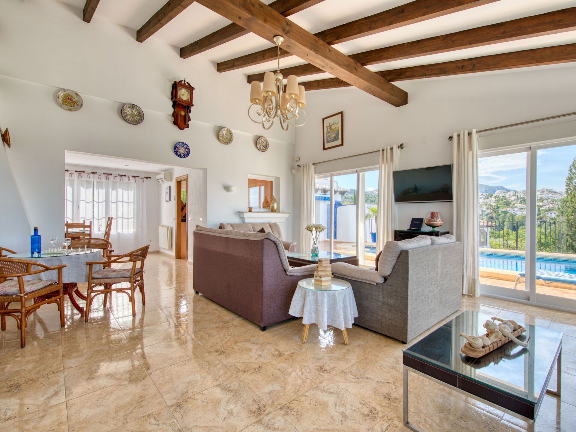 A spacious living area with a dining table, sofas, and a large window offering a view of a pool and landscape.