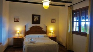 Un dormitorio con una cama de madera, dos lámparas de noche, un cuadro enmarcado en la pared y una ventana con cortinas.