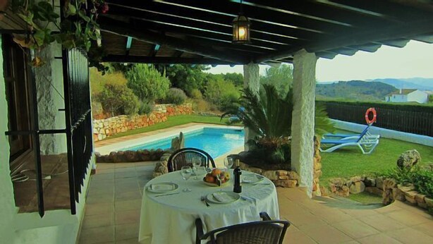 Un patio exterior con piscina, paredes de piedra y vistas del paisaje circundante.